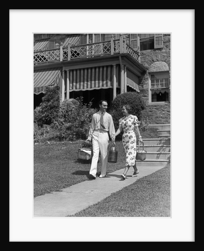1930s couple walking out of house down sidewalk carrying picnic baskets & thermos jug by Anonymous