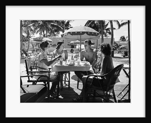 1930s three women and one man sitting at tropical pool side table talking together by Anonymous