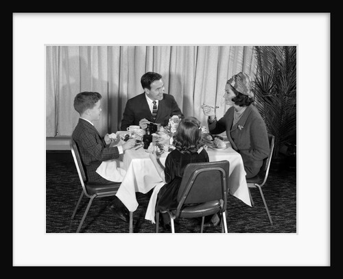 1960s smiling happy family of four eating meal in restaurant dad talking to mom who is wearing turban style hat by Anonymous