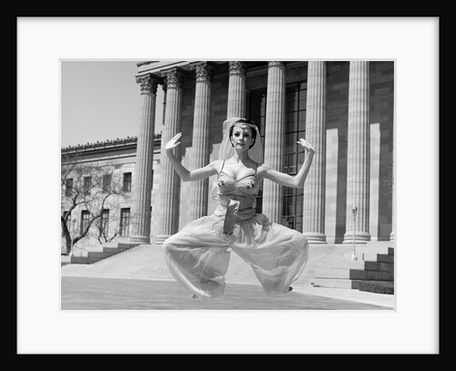 1960s woman in middle eastern belly dance costume jumping in front of building with greek style columns looking at camera by Anonymous
