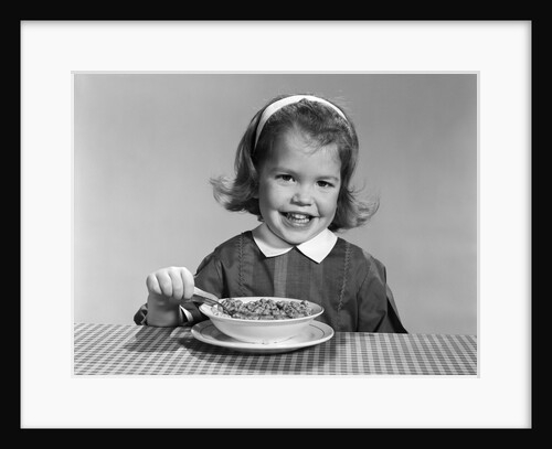 1950s 1960s smiling little girl eating a bowl of breakfast cereal looking at camera by Anonymous