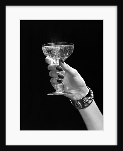 1930s 1940s 1950s woman hand ornate metal bracelet holding up new year toast glass of champagne against black background by Anonymous