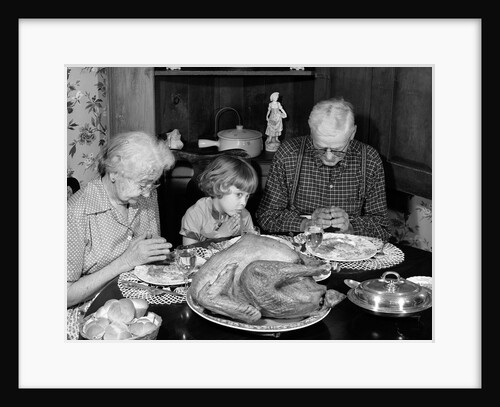 1950s 1960s little girl look at turkey sitting between grandmother grandfather saying grace at table by Anonymous