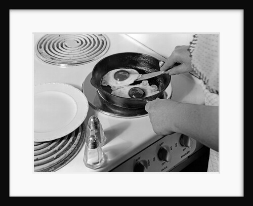 1940s 1950s woman hands frying eggs in iron skillet on electric stove salt and pepper shakers by Anonymous
