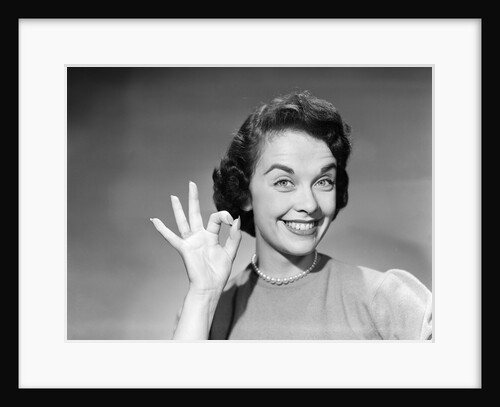 1950s woman smiling wearing pearl necklace looking at camera making okay gesture with hand by Anonymous