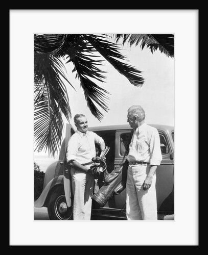 1930s 2 elderly men standing by car carrying golf bag palm tree frond in corner by Anonymous