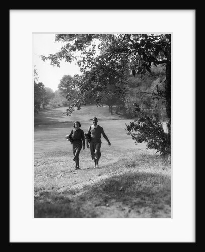 1930s couple man woman each carrying a golf bag walking down the fairway of the golf course by Anonymous