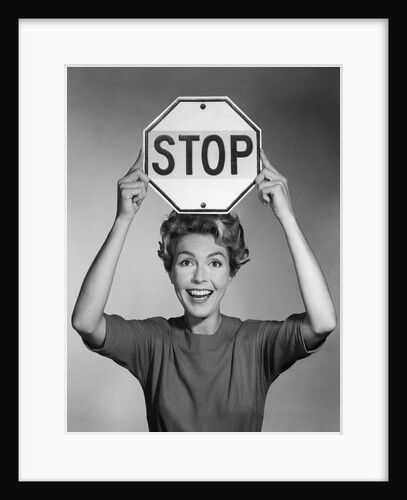 1950s 1960s smiling woman holding stop sign above her head looking at camera by Anonymous