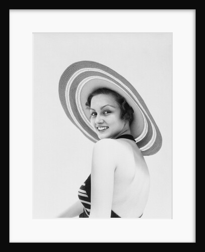 1930s woman wearing striped halter top and very wide brim straw hat looking at camera over shoulder by Anonymous