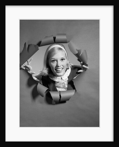 1960s blond woman breaking through ripped paper looking at camera smiling wearing headband by Anonymous