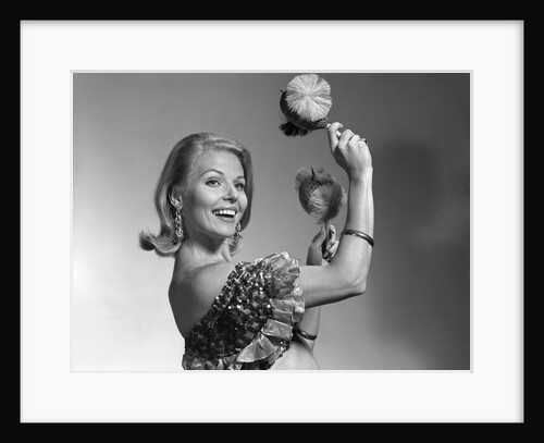 1960s smiling blond woman looking at camera shaking noise makers in her hands wear ruffled halter top by Anonymous