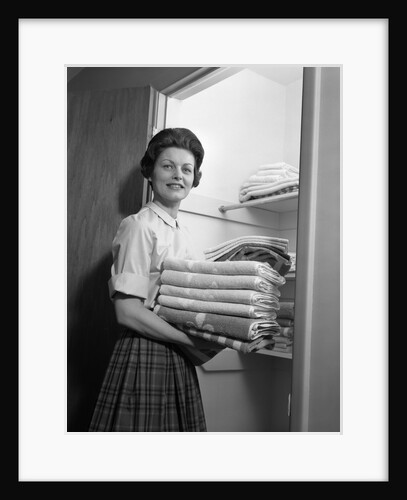 1950s 1960s housewife holding laundry folded towels by linen closet looking at camera by Anonymous
