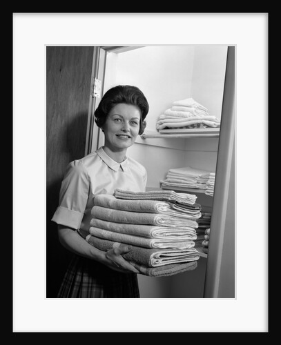 1960s woman holding laundry folded towels by linen closet looking at camera by Anonymous