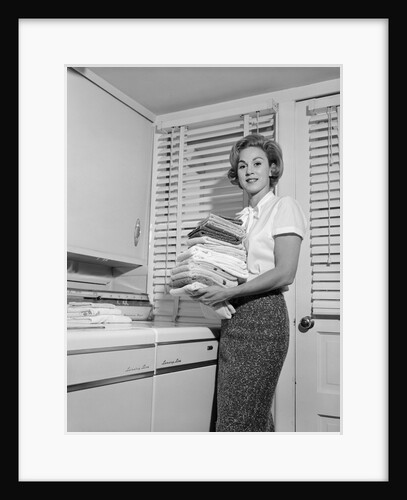 1960s woman holding folded laundry looking at camera by Anonymous
