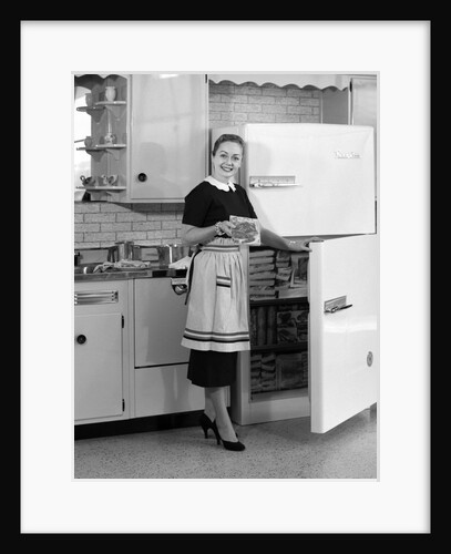 1950s smiling woman housewife in kitchen taking frozen food out of refrigerator freezer by Anonymous