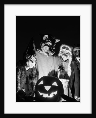 1960s group of four children in halloween costumes gathered around jack-o'-lantern indoor by Anonymous