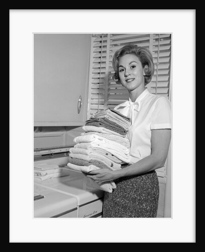 1960s smiling woman holding folded laundry looking at camera by Anonymous