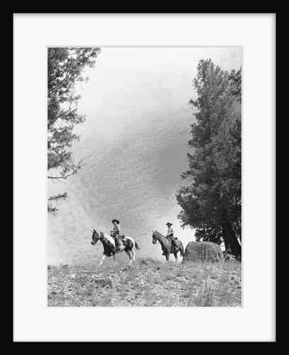 1950s 1960s two men on horseback riding across field wearing cowboy hats by Anonymous