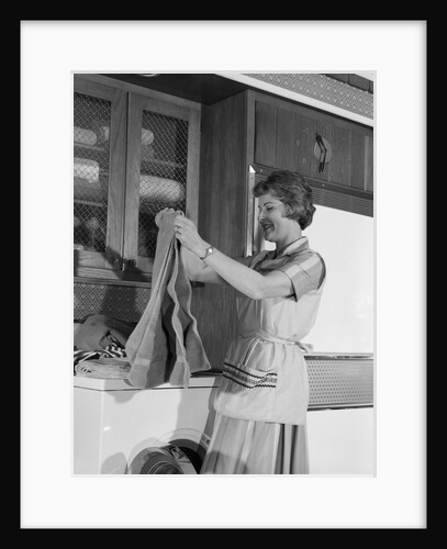 1960s woman folding laundry towels on dryer in kitchen by Anonymous