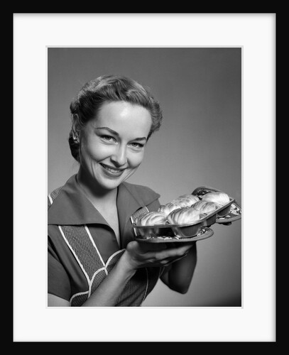1950s smiling woman holding freshly baked rolls looking at camera by Anonymous