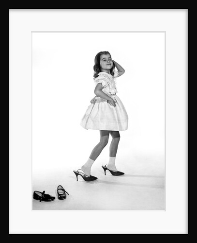 1960s girl making glamour pose having stepped out of her shoes into her mothers adult high heels by Anonymous