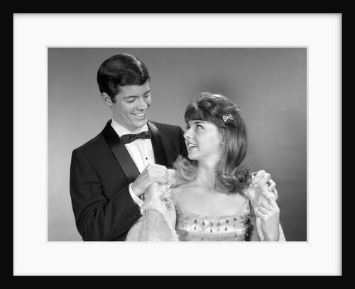 1960s teen couple formally dressed boy helping girl on with coat to go to prom by Anonymous