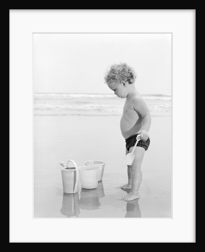 1960s 1970s child toddler standing in sand water bucket shovel by Anonymous