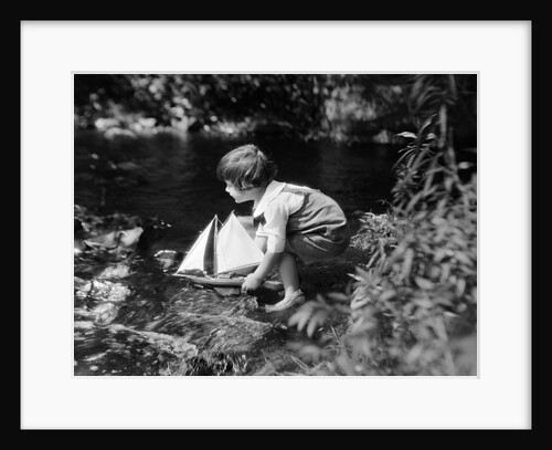 1920s boy putting toy sailboat into stream by Anonymous