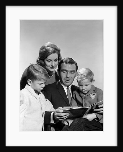 1960s family father mother sons reading book together by Anonymous