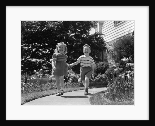 1950s two children holding hands smiling walking along sidewalk by Anonymous
