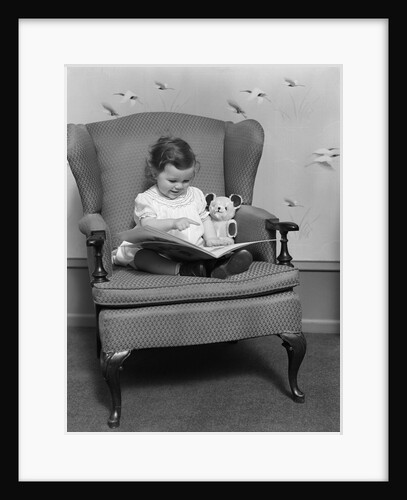 1930s little girl child in large chair with bear reading book by Anonymous
