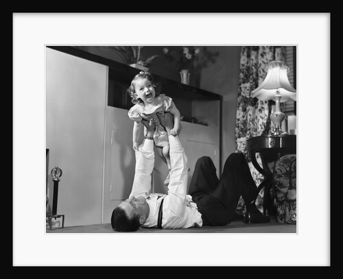 1950s father lying floor holding daughter girl up in the air by Anonymous