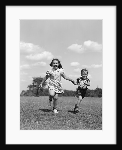 1940s two smiling children running holding hands in grassy field by Anonymous