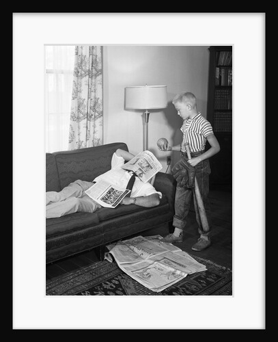 1950s father lying on a sofa with newspaper over his head while son is standing over him with bat ball and baseball glove by Anonymous