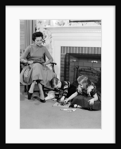1950s mother watching son daughter playing game in front of fireplace by Anonymous