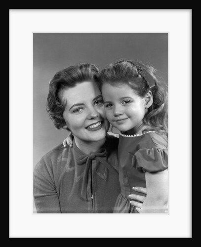 1950s girl daughter smiling hugging woman mother cheek to cheek together by Anonymous