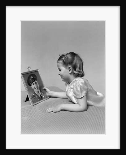 1940s child little girl looking at framed picture of her father a soldier in uniform by Anonymous