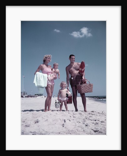 1950s family man woman mother father children boy girl son daughter standing sandy beach with toys and picnic basket by Anonymous