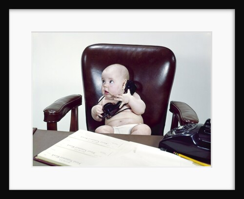 1960s chubby baby sitting in leather chair at office desk holding telephone by Anonymous