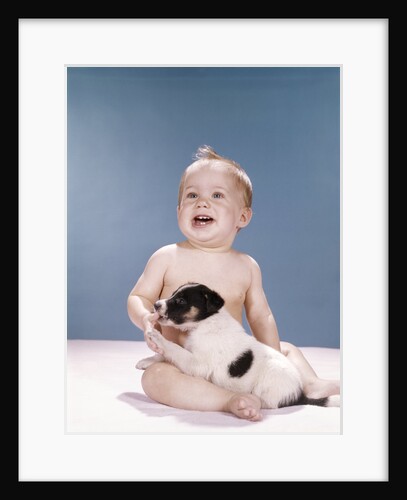 1960s smiling baby girl sitting in diapers playing with young black and white puppy dog by Anonymous
