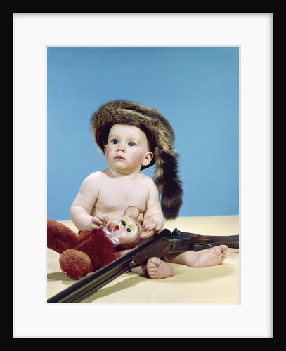 1960s baby boy wearing coonskin cap with stuffed animal and shotgun gun by Anonymous