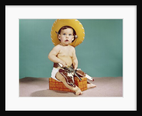 1960s baby wearing cowboy hat and holster with guns pistols looking at camera by Anonymous