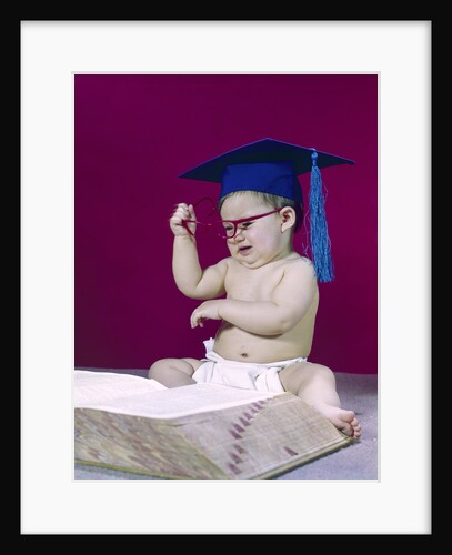 1960s graduate baby wearing mortarboard eyeglasses reading book by Anonymous