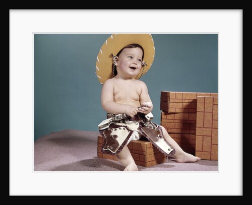 1960s smiling baby wearing cowboy hat and cap pistols and western holsters by Anonymous