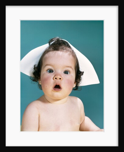 1960s surprised baby facial expression wearing a nurse cap looking at camera by Anonymous