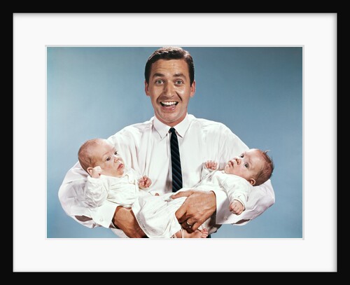 1960s smiling man father looking at camera holding twin babies infants by Anonymous
