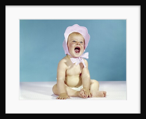 1960s baby wearing pink checked bonnet laughing by Anonymous