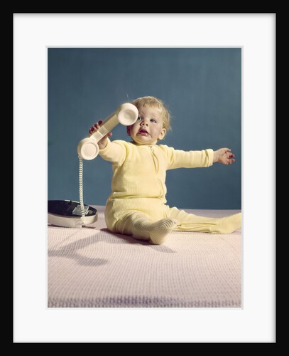 1960s baby holding telephone head set by Anonymous