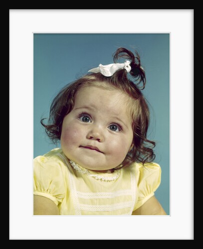 1960s brunette baby girl round chubby face yellow dress ribbon topknot interested sincere facial expression looking at camera by Anonymous