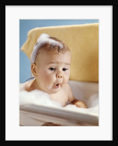 1960s baby with a surprised facial expression in bathtub covered with soap bubbles by Anonymous